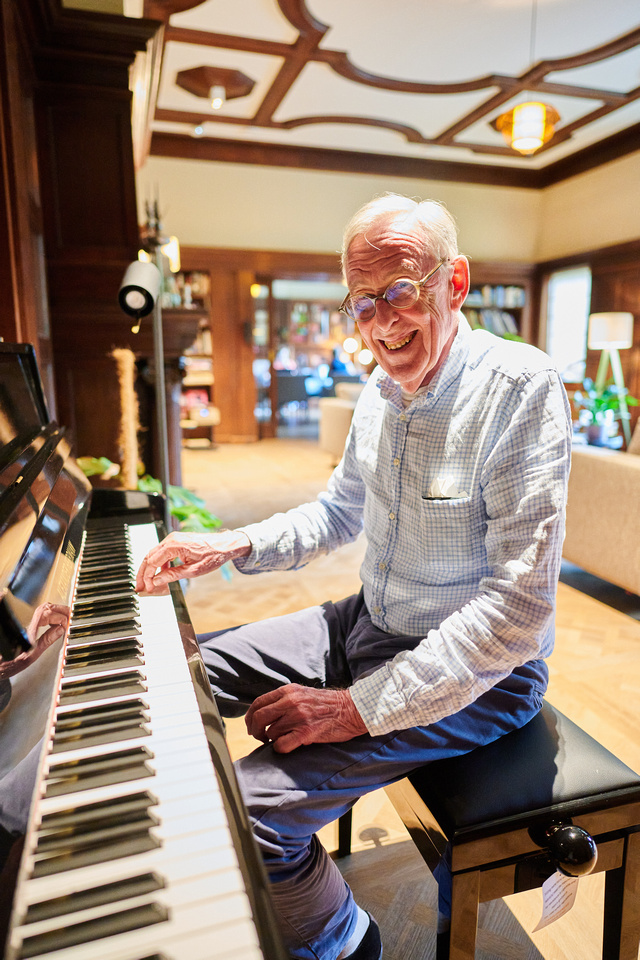 Oudere man speelt piano en lacht in de camera